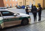 Funkcjonariusze KAS prowadzą zatrzymaną osobę. 2 samochody służbowe.