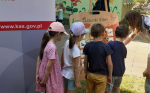 Funkcjonariuszka pokazuje dzieciom zagrożone gatunki na planszy. Po lewej stronie baner z adresem www.kas.gov.pl