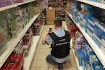 Korytarz sklepowy. Funkcjonariusz Służby Celno-Skarbowej robi zdjęcie zabawkom ułożonym na regałach sklepowych
