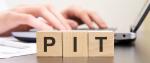 drewniane klocki z literami PIT, w tle laptop i ręce