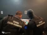 Dwóch funkcjonariuszy służby celno-skarbowej stoi przed ekranem monitora wykorzystywanego do nielegalnych gier hazardowych.