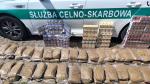 auto służbowe Służby Celno-Skarbowej, przed  samochodem ułożone worki z nielegalnym tytoniem do palenia i paczki papierosów