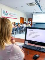 Grupa przedsiębiorców siedzi na sali i słucha prezentacji, którą przedstawia urzędniczka