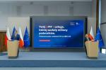 Minister Marcin Łoboda stoi po lewej stronie sali, za mównicą, na konferencji. W tle flagi Polski i Unii Europejskiej.