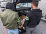 Funkcjonariusz Służby Celno Skarbowej i funkcjonariusz Policji przeszukują bagażnik samochodu